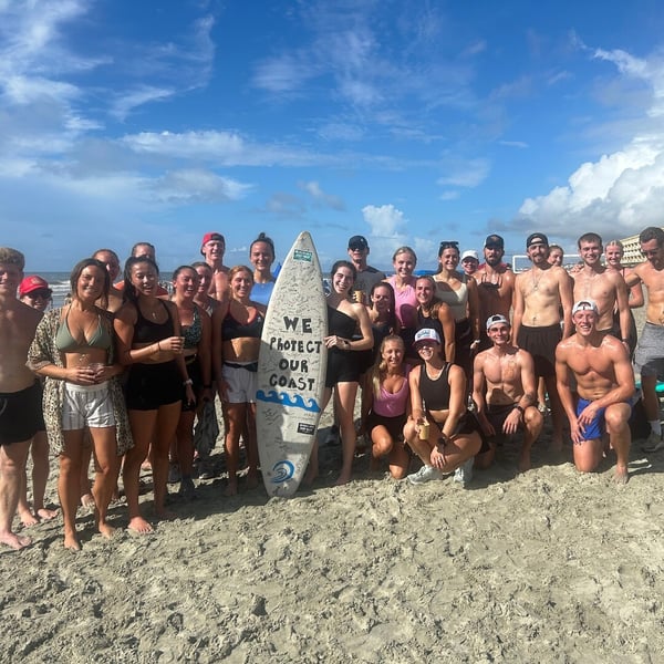 Volunteers pose on Folly Beach with surfboard that states 